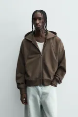 Sudadera con capucha y cierre de cremallera frontal, color marrón oscuro, de corte holgado (boxy fit) y manga larga. Presenta bolsillos frontales de vivo y acabados en rib en puños y bajo.