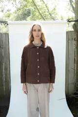 Cardigan de punto color marrón, abierto con botones imitación hueso, manga larga con parche bordado y diseño texturado.