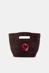 Mini bolso de mano tejido en rafia color marrón oscuro, con diseño estructurado y detalle de flor decorativa en tonos rojizos realizada en crochet.