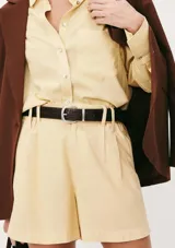 Short de corte recto y tiro alto, confeccionado en tela de lino color amarillo claro. Presenta cintura con elástico en la parte posterior, trabillas para cinturón y bolsillos laterales.