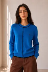 Cardigan de punto azul con ribetes en contraste negro, cuello redondo, cierre frontal con botones y bordado pequeño en el pecho.