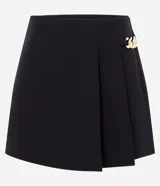 Short pollera de sastrería marca Cortelle, color bordó, confeccionado en crepé. Presenta sobreposición frontal efecto pollera con pliegues y detalle de cadena metálica decorativa en el lateral.