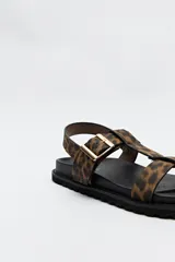 Sandalia plana con estampado animal, base de goma dentada y hebilla metálica ajustable.