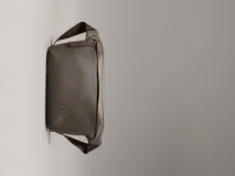 Riñonera de poliuretano color gris topo, con textura granulada y logo 'CK' grabado en el frente. Posee una correa ajustable de tela marrón oscuro.