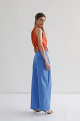 Top sin mangas color naranja, con cuello halter y abertura en el delantero y espalda. Detalle de fruncido en el cuello y ruedo que se ajusta y cierra con lazo en contraste color azul.