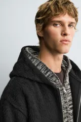Sobrecamisa de corte relajado confeccionada en tejido con textura efecto pelo. Presenta cuello con capucha, manga larga, bolsillos laterales y cierre frontal con cremallera.