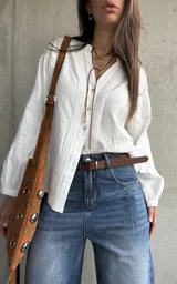 Camisa blanca de manga larga con detalles bordados en las mangas y encaje en el frente y hombros, escote en V con botones frontales.