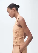 Top de cuello halter color salmón, con diseño entallado y detalle de fruncido lateral. Presenta cierre de botones en el cuello y cierre de cremallera lateral.