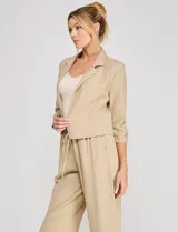 Blazer corto de lino color beige, marca Allie Rose, de estilo relajado y corte crop con frente abierto sin botones. Presenta solapa de muesca y mangas tres cuartos con detalle fruncido en los laterales.
