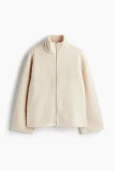 Campera oversized de sherpa suave color beige, con cuello elevado, cierre frontal y bolsillos discretos en las costuras laterales. Presenta hombros caídos y mangas largas amplias.