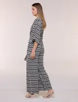Enterito de calce relajado con caída fluida, escote en V cruzado estilo wrap, mangas tres cuartos estilo kimono y pantalón wide leg. Cuenta con cinto textil a tono para anudar en la cintura y bolsillos laterales, con diseño estampado geométrico en blanco y negro.