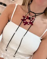 Choker largo de tiento negro con dije central de acrílico color bordó en forma de sol irregular, decorado con apliques de strass. El diseño incluye detalles de cuentas metálicas plateadas a lo largo de los cordones.