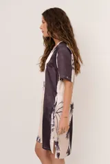 Vestido corto de corte recto y holgado, con mangas cortas y cuello redondo. Presenta un diseño estampado con motivos florales oscuros y una franja lateral en tono contrastante.