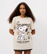 Remera de algodón color beige con cuello redondo y mangas cortas. Presenta una estampa frontal centrada del personaje Snoopy sosteniendo una taza y una dona, acompañada por el texto 'Snoopy's Coffee & Treats'.