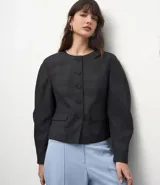 Blazer de sastrería color gris con estampado de cuadros, cuello redondo y cierre frontal con botones forrados. Presenta mangas largas con volumen tipo baloné y bolsillos frontales con solapa.