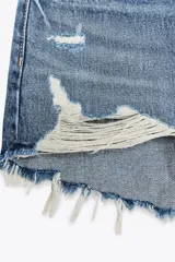 Short de jean negro desgastado, tiro alto, con roturas pronunciadas y terminación deshilachada en el bajo. Presenta cinco bolsillos y cierre frontal con botón metálico.