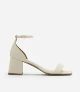 Sandalia de tacón color crema, con puntera cuadrada, tira delgada sobre los dedos y tobillo con hebilla. El tacón es geométrico y mide 7 cm de altura.