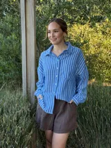 Camisa celeste con rayas verticales blancas, de manga larga, cuello camisero y cierre frontal con botones.