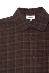 Camisa de corte boxy confeccionada en franela a cuadros, con cuello clásico, cierre frontal de botones, bolsillo en el pecho y puños abotonados.