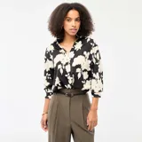 Blusa de corte fluido con estampado floral en contraste, cuello camisero, cierre frontal de botones y mangas tres cuartos.