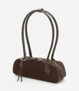 Cartera tipo shoulder bag de tamaño pequeño y formato alargado, confeccionada en material sintético efecto gamuza. Cuenta con asas de hombro estructuradas, cierre superior con cremallera y detalles metálicos decorativos.