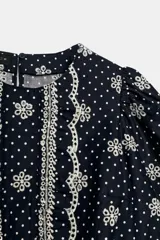 Blusa azul marino con estampado de lunares blancos, cuello redondo y mangas abullonadas. Presenta detalles de bordados perforados, volantes delanteros y acabados elásticos.