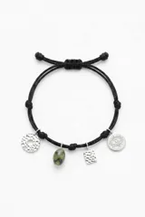 Pulsera de cordón negro ajustable con cuatro dijes colgantes: un círculo texturizado, una piedra verde, una placa rectangular texturizada y un dije circular con diseño de ojo.