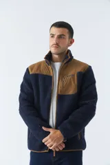 Campera de sherpa para hombre, color azul marino con detalles en marrón. Tiene cuello alto, cierre frontal y bolsillos laterales con cierre.