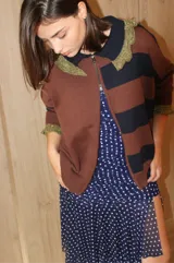 Cardigan de tejido de punto con diseño a rayas horizontales en tonos marrón y azul marino. Presenta cierre frontal con doble cursor, cuello tipo polo con detalles en hilo metalizado dorado y puños con el mismo acabado brillante.