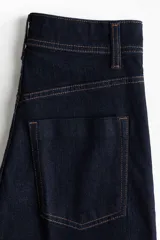 Jean wide leg de tiro alto en denim azul oscuro con costuras en tono contraste, trabillas para cinto y cierre frontal con botón metálico.