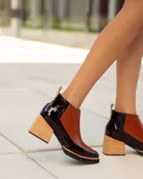 Botinetas de cuero con diseño bicolor, combinando paneles en color negro y marrón con textura de reptil. Presentan un taco cuadrado de madera y suela con plataforma.