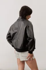 Chaqueta de cuero color negro, de corte oversize, con cierre frontal y solapas.