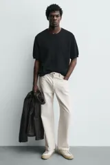 Zapatilla deportiva de estilo retro, color blanco con detalles en gris y negro. Presenta una suela de color beige en contraste y cordones blancos.