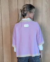 Buzo de lana lambswool en color lila, con cuello redondo, puños y ruedo en tono beige contrastante. Presenta un diseño holgado de manga corta con terminación acanalada.