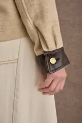 Campera corta de paño color marrón con detalles en cuero sintético al tono en cuello, puños y solapas de bolsillos. Presenta cierre frontal con botones metálicos dorados y dos bolsillos frontales tipo cargo.