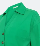 Camisa de manga corta confeccionada en mezcla de viscosa y lino color turquesa. Presenta cuello camisero con escote en V, bolsillos frontales de parche y cierre frontal con botones geométricos de efecto carey.