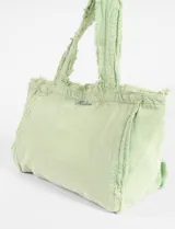 Bolso tipo tote de algodón con efecto lavado, diseño con bordes desflecados y asas fijas. Presenta un pequeño bordado decorativo en la parte frontal.