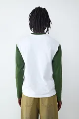Remera de manga larga con diseño estilo camiseta de fútbol, cuerpo blanco y mangas verdes. Presenta estampados gráficos en el frente con la inscripción 'Victory Legend', el número '39' y un emblema ovalado.
