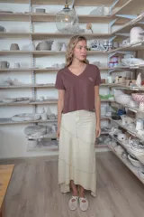Falda larga de lino color beige, de corte asimétrico con costuras decorativas pespunteadas en contraste y diseño envolvente con bajo más largo en la parte trasera.