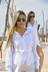 Camisa blanca de manga larga con cuello clásico, ajuste en la cintura mediante lazo del mismo tejido y hombros ligeramente abullonados.