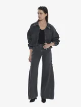 Chaqueta de denim color negro lavado, de calce regular y textura suave. Presenta cuello camisero, cierre frontal y mangas largas con puños ajustados con elástico.