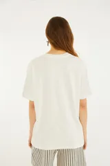 Remera blanca de manga corta y cuello redondo, con estampa frontal ilustrada de un paisaje de playa con la inscripción "Carioca".