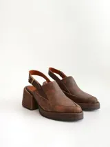 Zapato tipo zueco de cuero color chocolate con efecto desgastado, plataforma y taco cuadrado. Presenta una tira trasera ajustable con hebilla metálica.