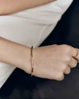 Brazalete rígido de oro de diseño ondulado y sutil, adornado con pequeñas circonitas blancas distribuidas a lo largo de la pieza.