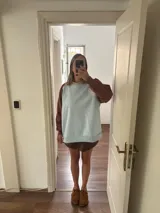 Buzo celeste con mangas marrones y bordado dorado en el frente.