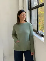 Sweater de punto color verde, de corte recto y holgado, con cuello redondo y dos bolsillos frontales aplicados.