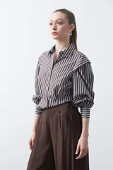 Camisa a rayas verticales blancas y marrones, de manga larga con puños ajustados y cuello camisero. Presenta un diseño con volados en los hombros y entalle en la cintura.