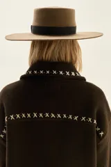 Campera de lana merino hervida en color crudo, con diseño de cuello camisero, cierre frontal de botones y bolsillos frontales. Presenta bordados artesanales con motivos geométricos en tonos marrón y azul en el frente, espalda y mangas.