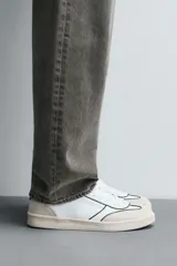 Zapatilla deportiva de estilo retro, color negro, con parte superior fabricada en combinación de piezas de cuero liso y gamuza perforada. Presenta una suela de goma en color marrón oscuro o ahumado en contraste.