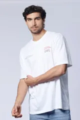 Remera blanca de corte oversize con estampado pequeño en el frente que incluye texto y dibujo.